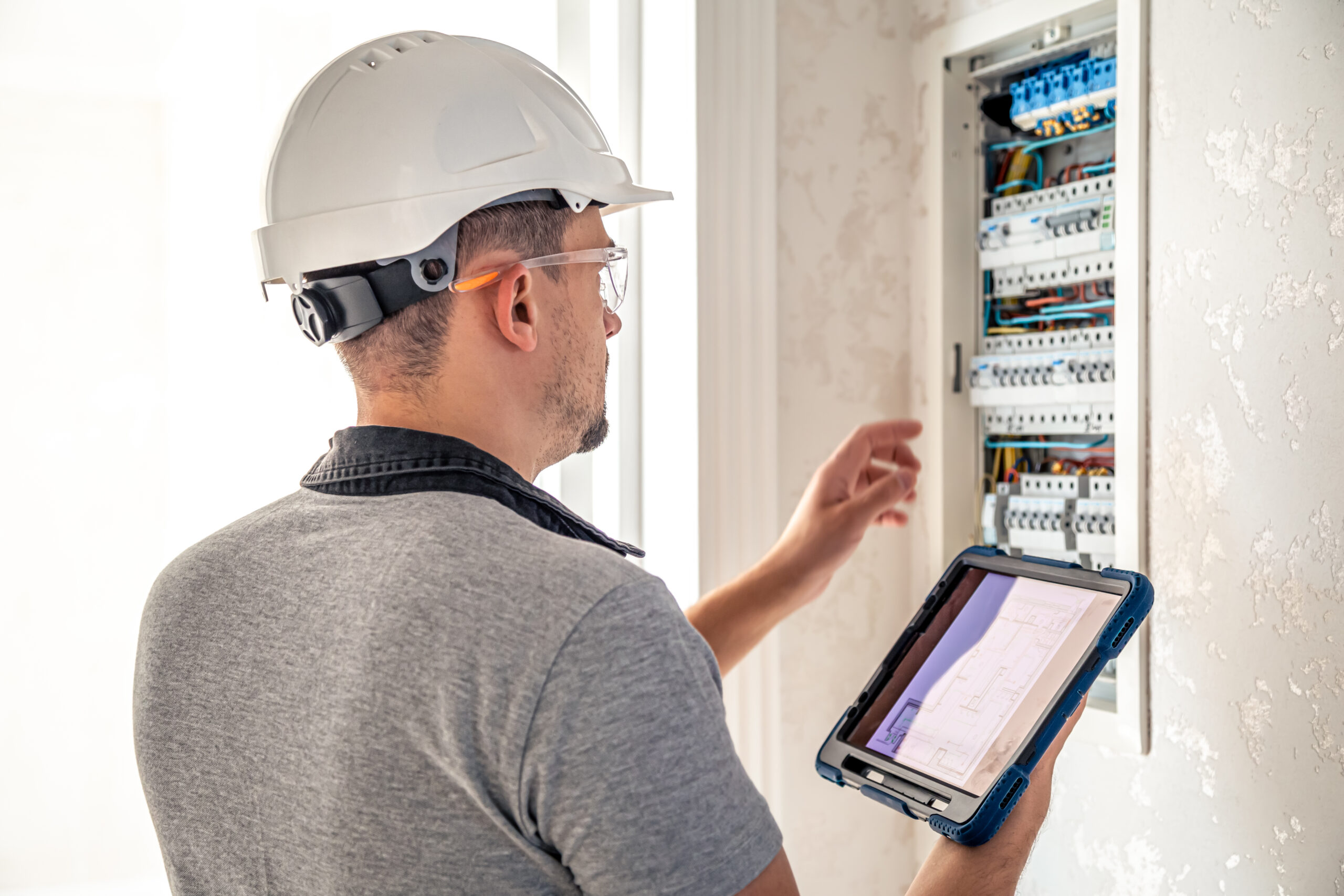 Man, an electrical technician working in a switchboard with fuses, uses a tablet.